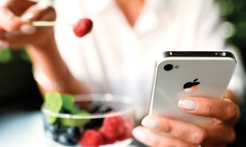 Mujer comiendo frutas postre con iPhone 4S en manos